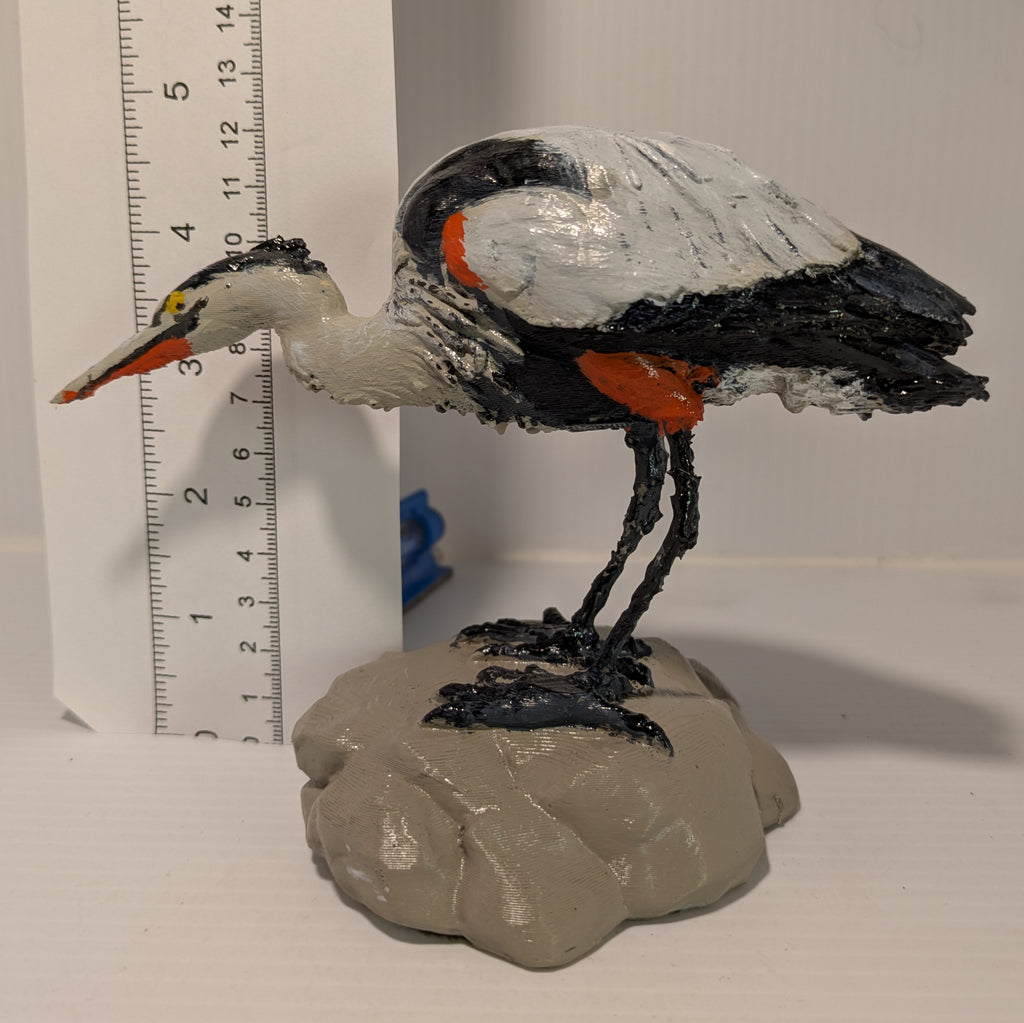 Decorative heron figurine on a rock with a ruler for scale