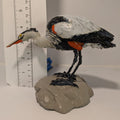 Decorative heron figurine on a rock with a ruler for scale