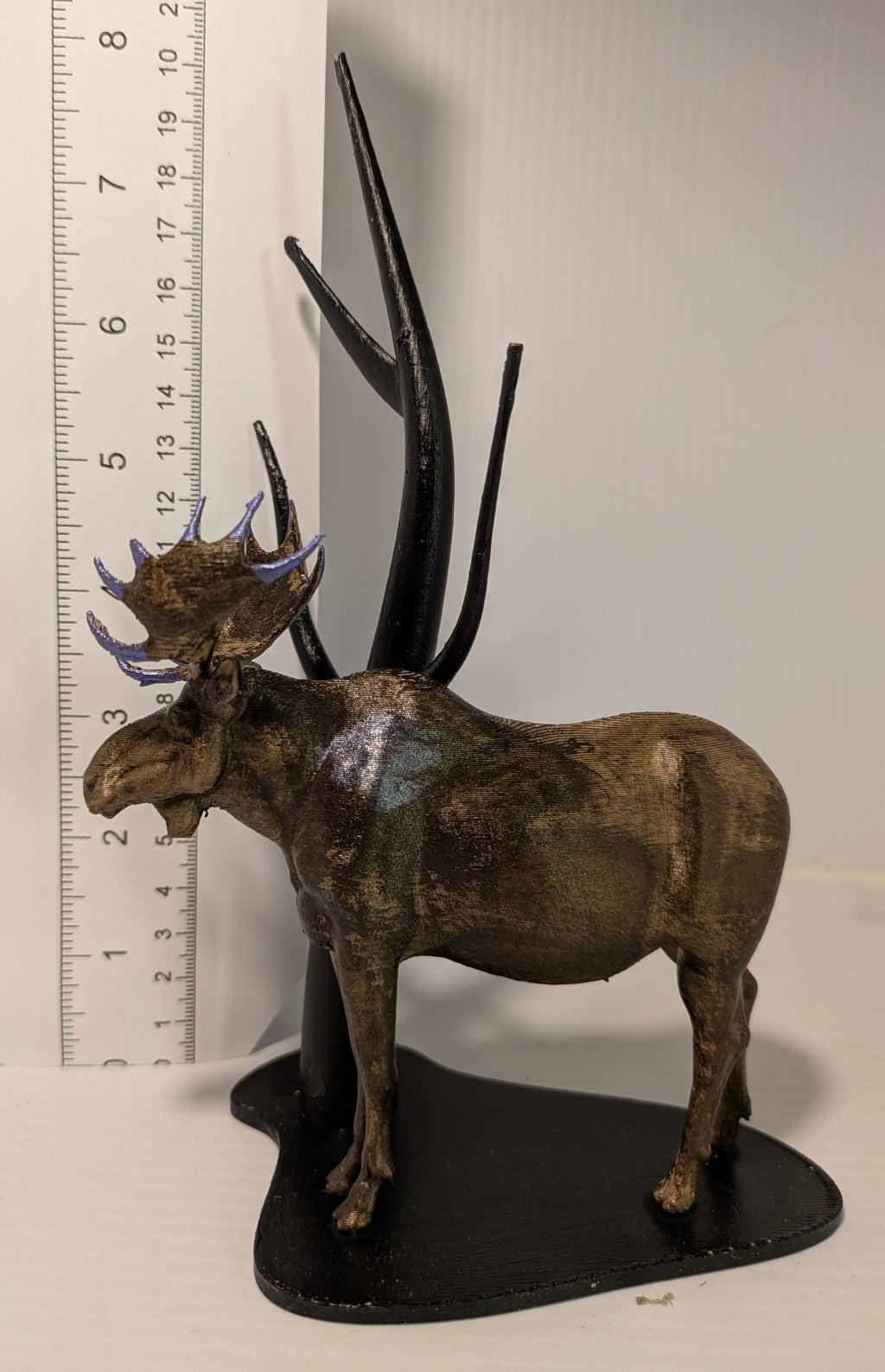 Metallic antelope figurine with large antlers next to a ruler on a white background