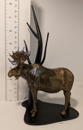 Metallic antelope figurine with large antlers next to a ruler on a white background