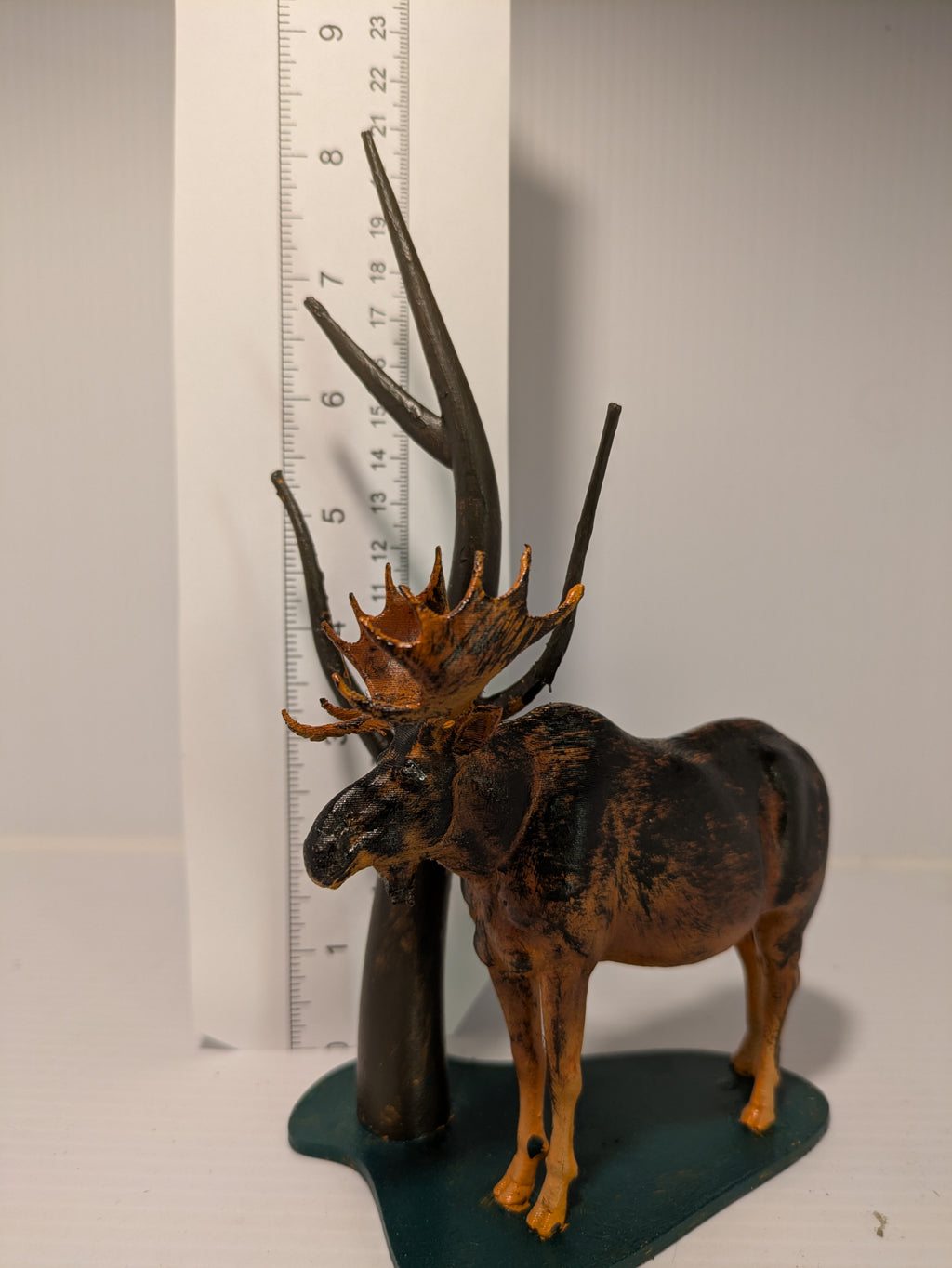 Model of a deer with large antlers next to a ruler on a plain background