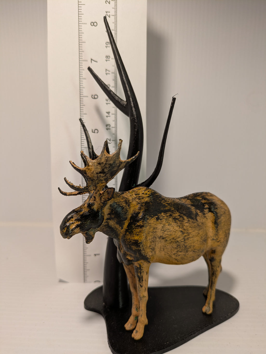 Decorative moose figurine with large antlers on a stand next to a ruler for scale.