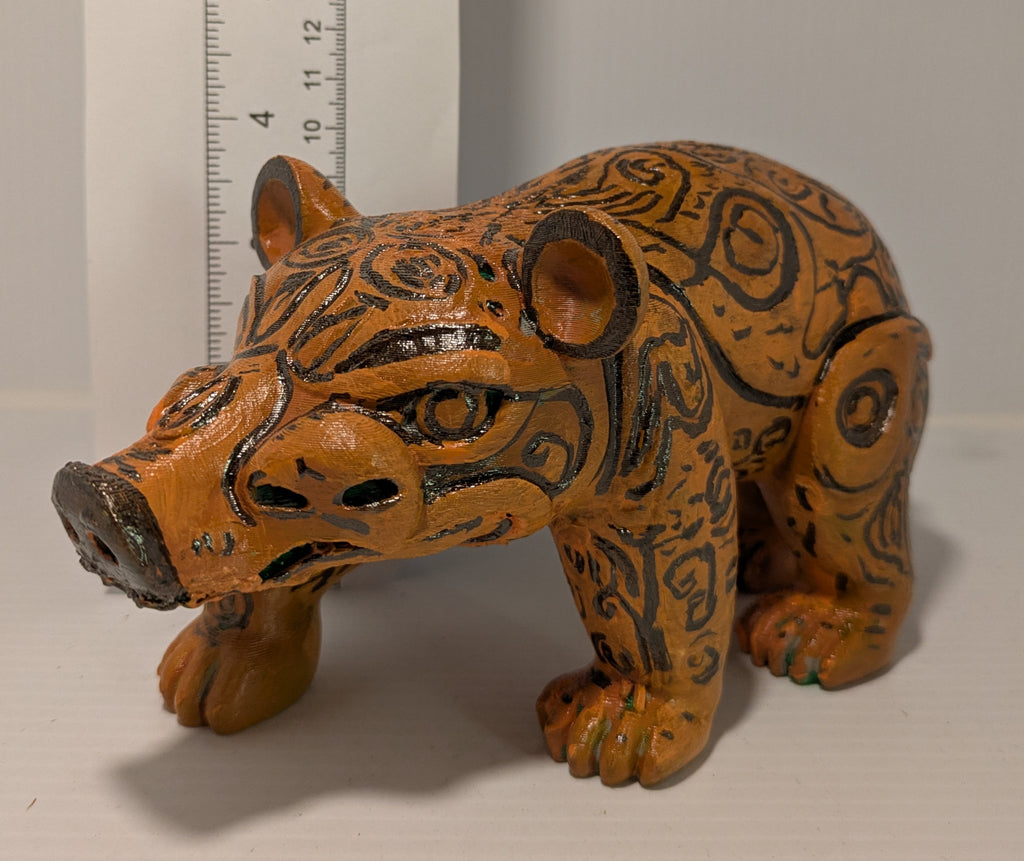 Decorative figurine of a stylized animal with tribal patterns next to a ruler for scale.